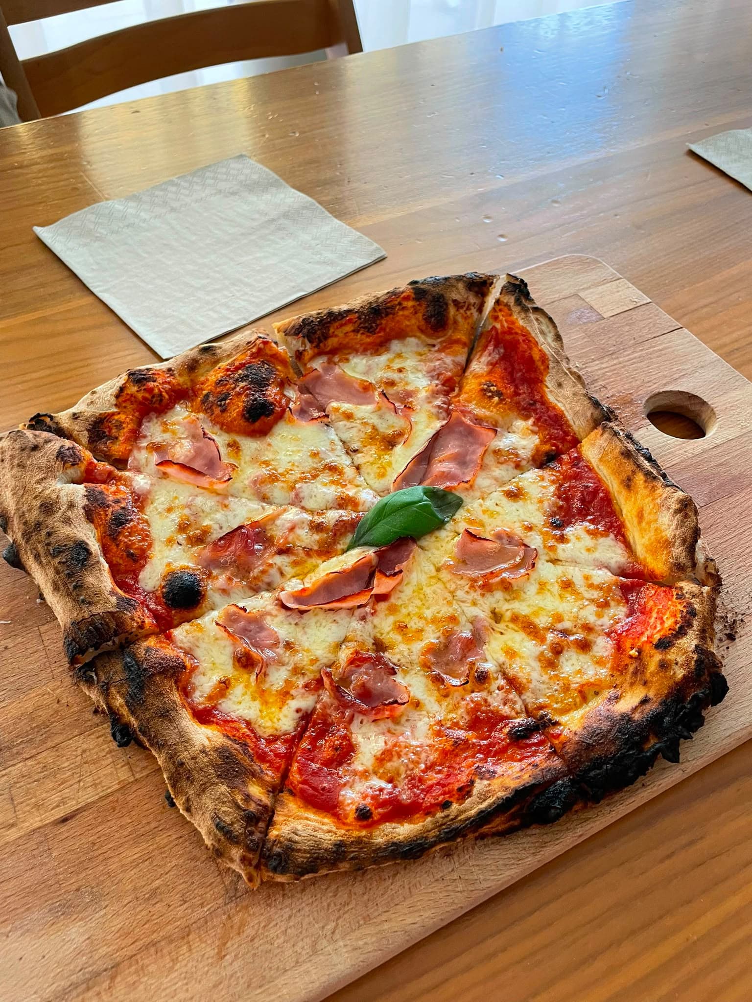 Frisch gebackene Pizza mit Prosciutto und Basilikum auf einem Holzbrett