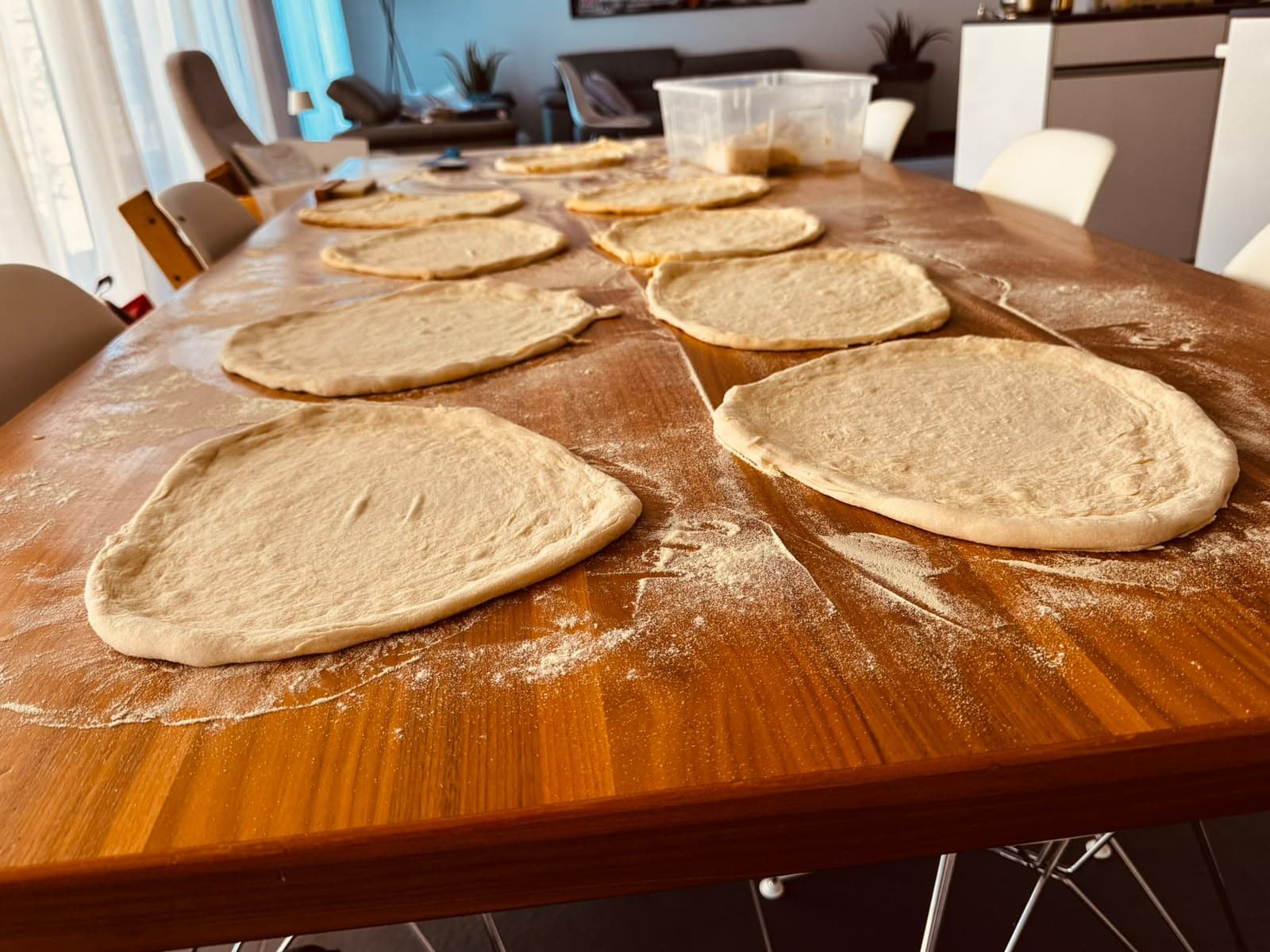 Von Hand geformte Pizzateigböden auf einem bemehlten Holztisch
